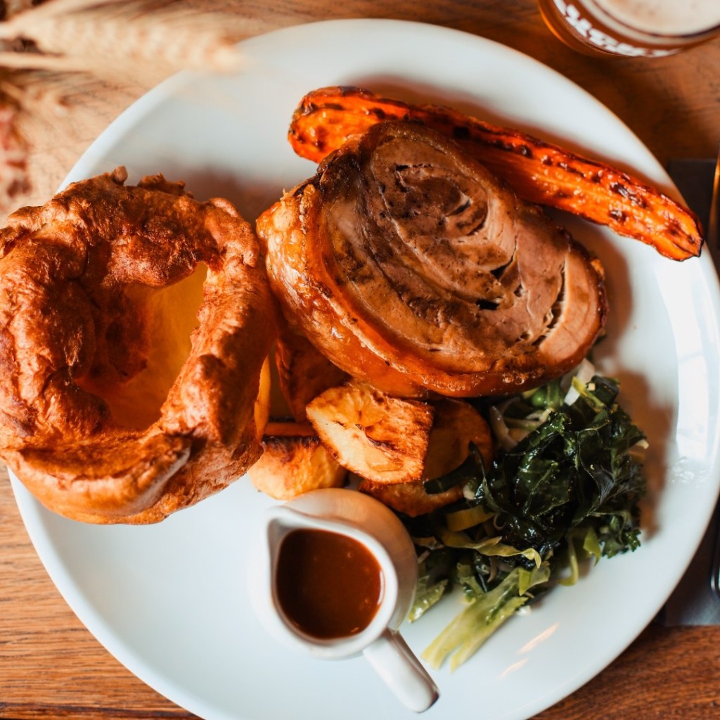 A porchetta roast served with a large Yorkshire pudding and vegetables at The Royal Oak in the Peak District.