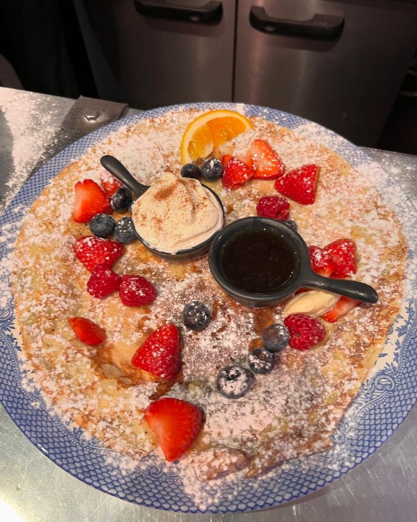 A large Dutch pancake served on a plate and covered in icing sugar, strawberries, ice cream and syrup. 