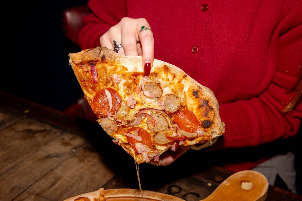 Person holding a slice of New York style pizza at Revolution in York. 