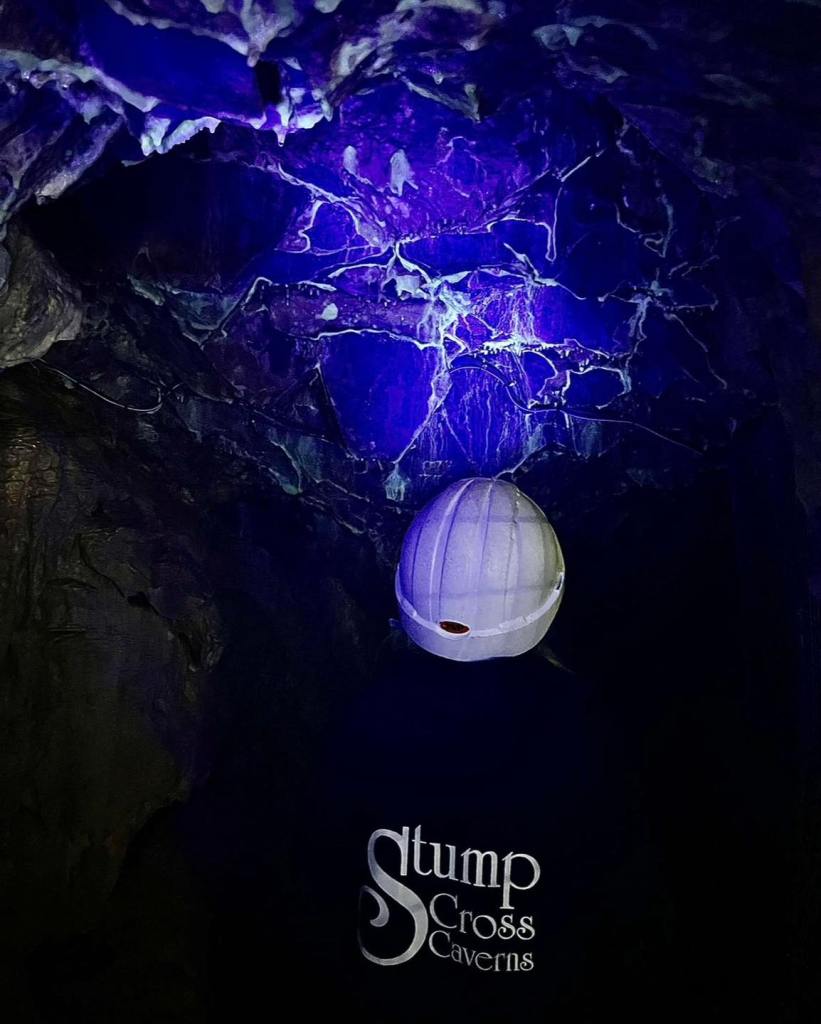 A person exploring Stump Cross Caverns in the dark with a UV light glowing the calcite. 