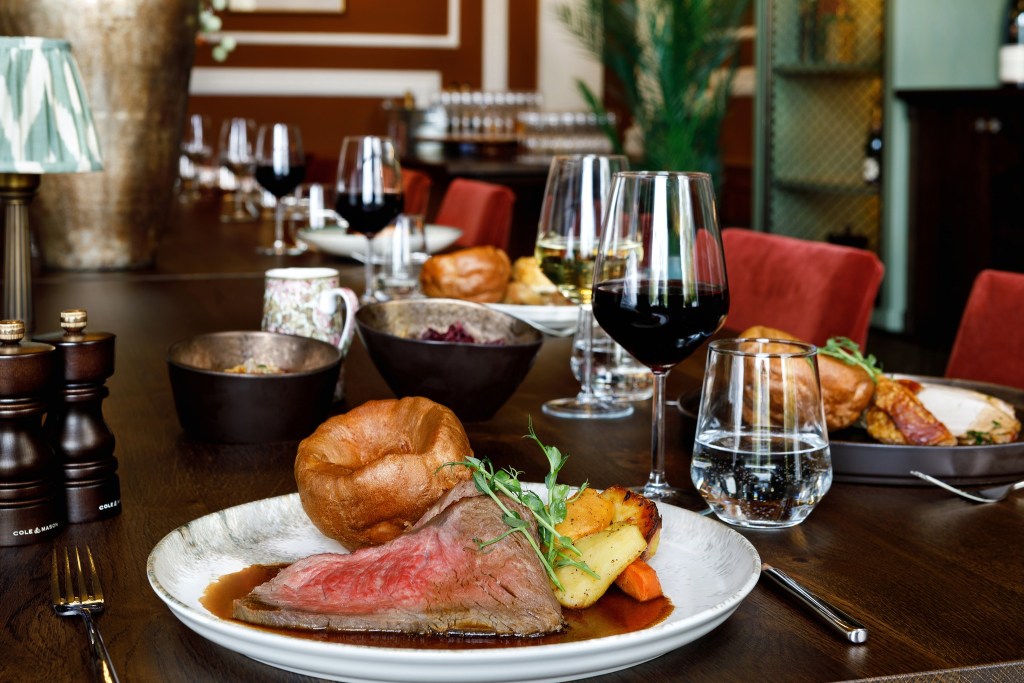 A sunday roast presented on a table with wine, with Yorkshire puddings and roast beef on display. 