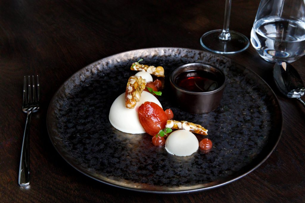 A white chocolate dessert presented fine dining style on a black plate. 