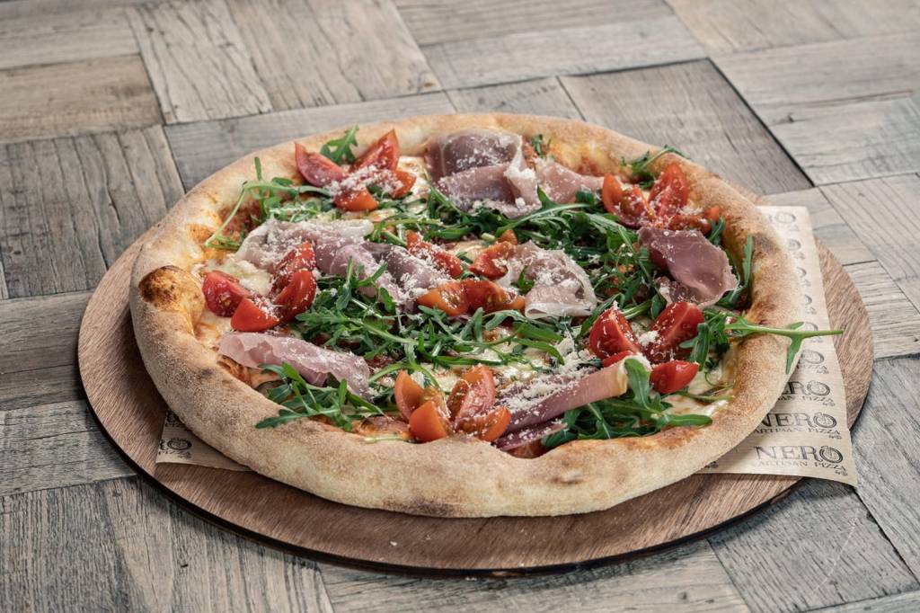 A Neapolitan-style pizza served on a wooden board, with ham and tomatoes on top. 