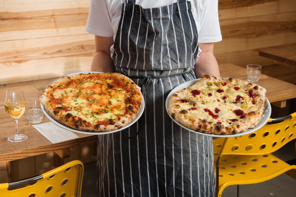 Two pizzas being held up by a server at Rind, Yorkshire Dales. 