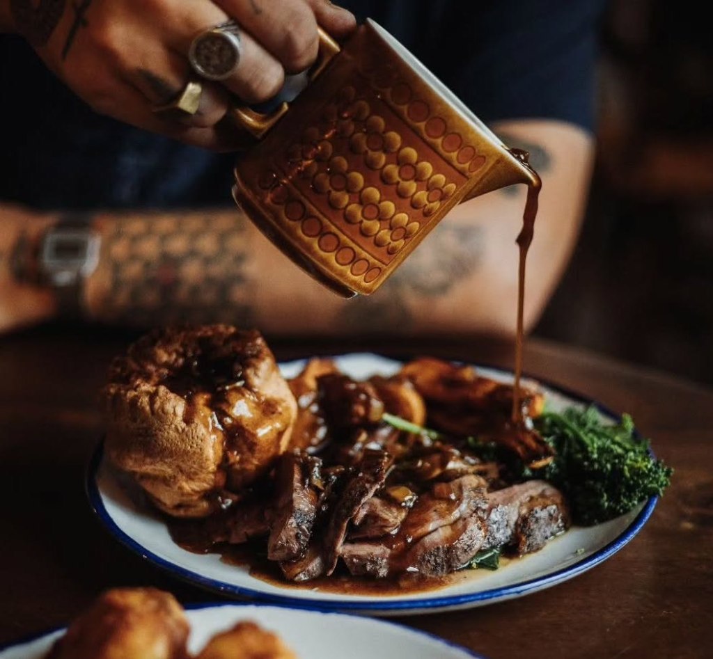 A Sunday roast on a table, while someone pours a jug of gravy over the food. 