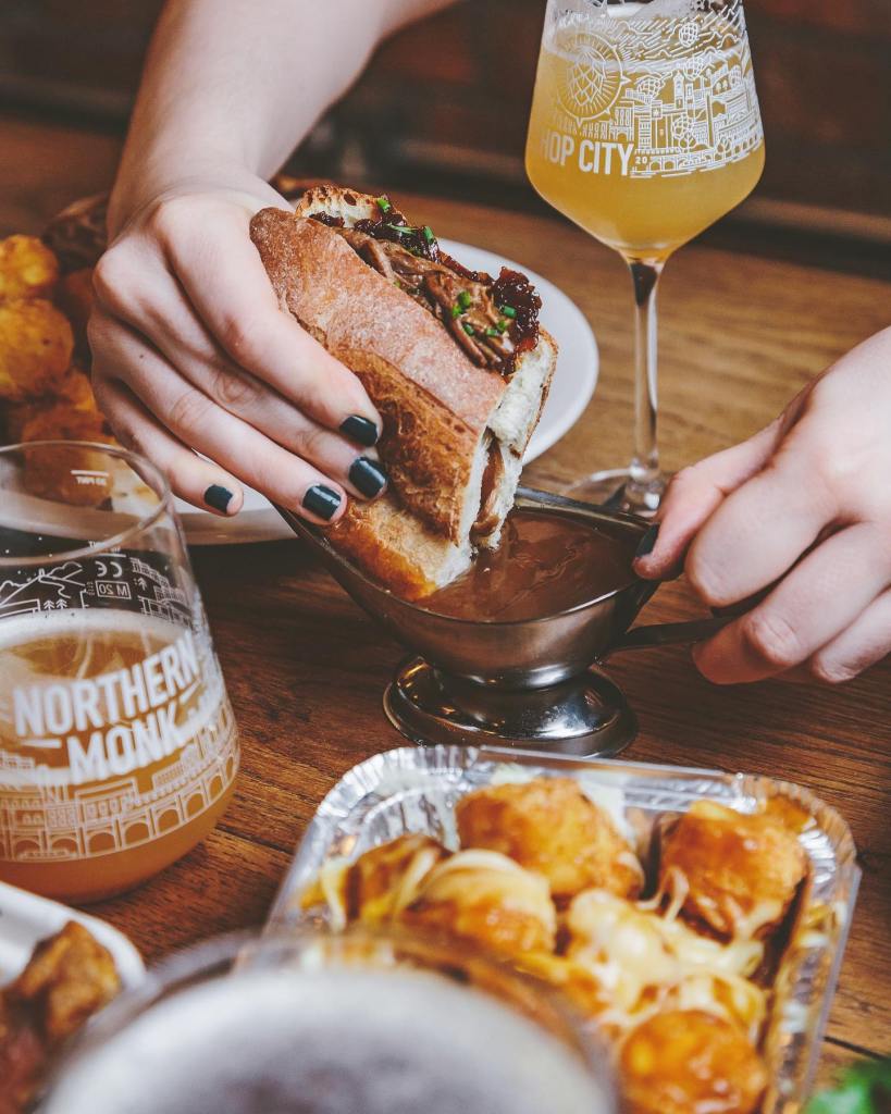 A sandwich held in a diner's hand, with a pint of beer sitting next to the plate. 